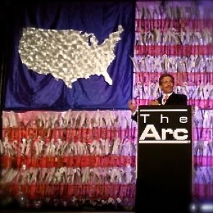 Be Involved_Story Flag Exhibit_photo of Geraldo giving keynote address in from of story flag about how he broke the story about the mistreatment of patients at the Willowbrook institution.